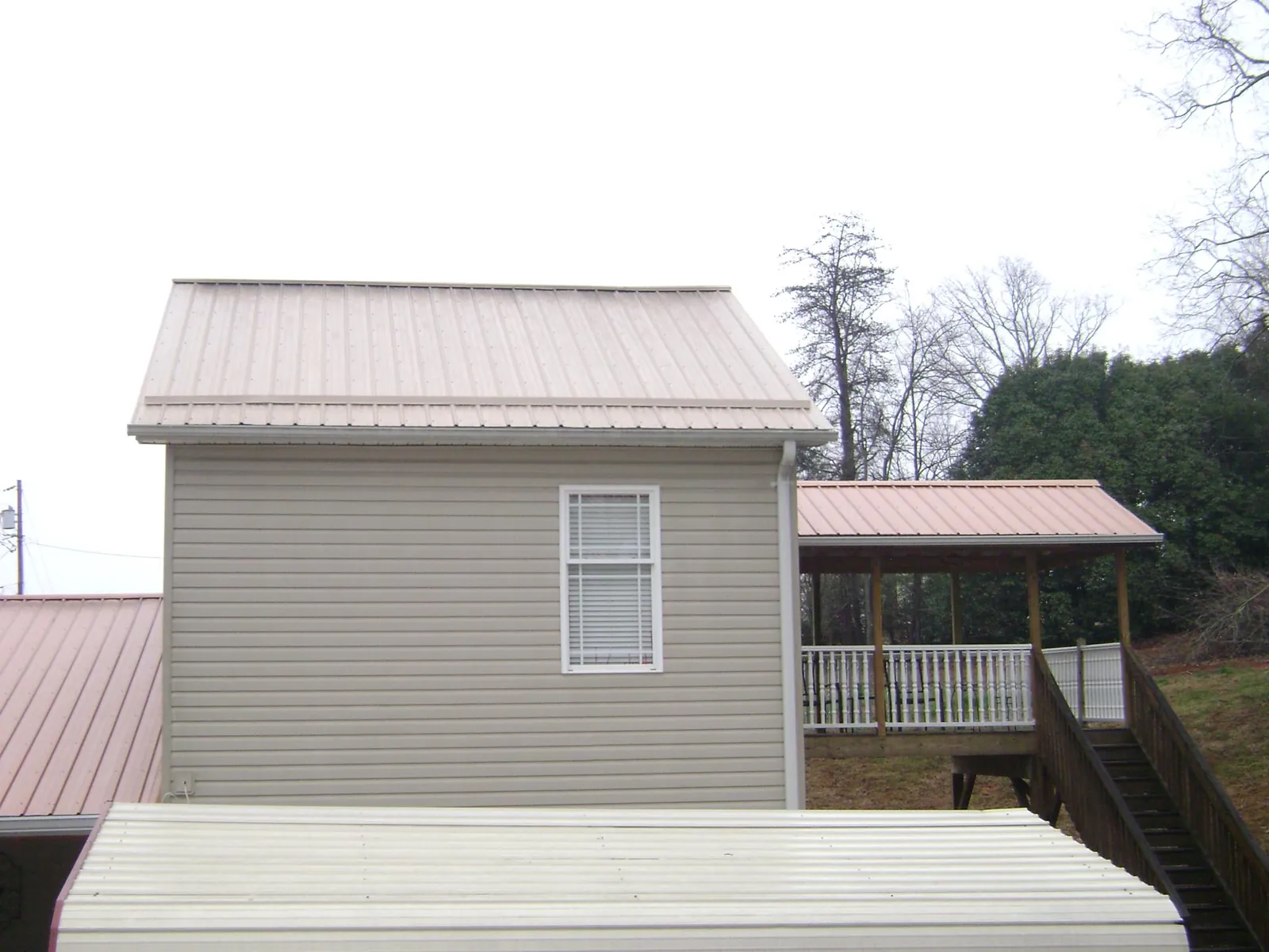 Tan metal roofs on a two story addition and attached porch, from a Roof Replacement job in Syracuse